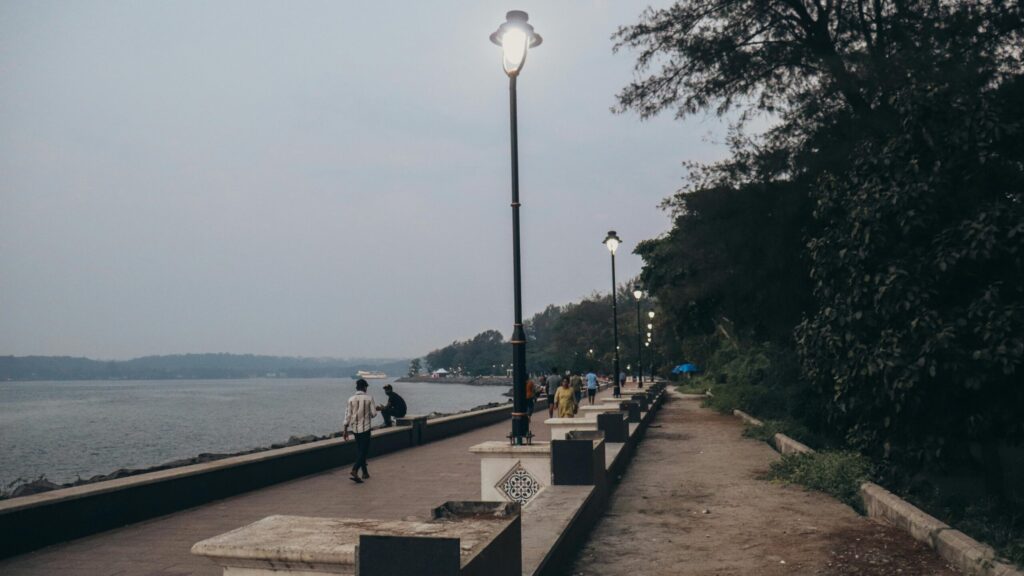 A tranquil riverside promenade with streetlights, trees, and people walking.
