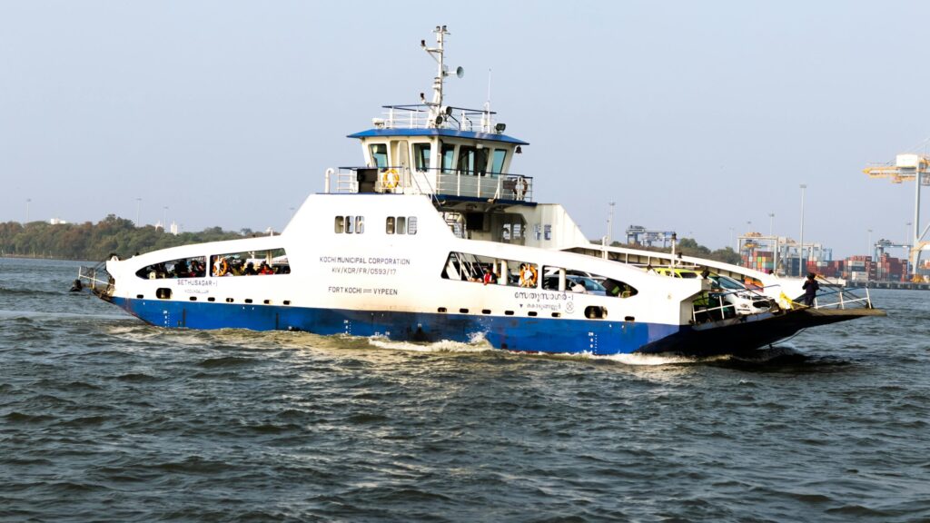 Blue and white ferry navigating through the waters of Kochi, India under a clear sky.